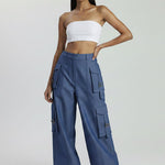 Woman wearing a white strapless top and blue cargo pants on a light gray background