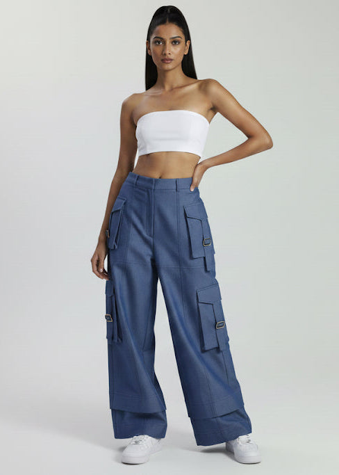 Woman wearing a white strapless top and blue cargo pants on a light gray background