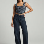 Woman wearing a patterned top and dark jeans on a gray background