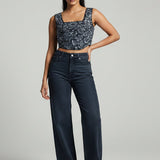 Woman wearing a patterned top and dark jeans on a gray background