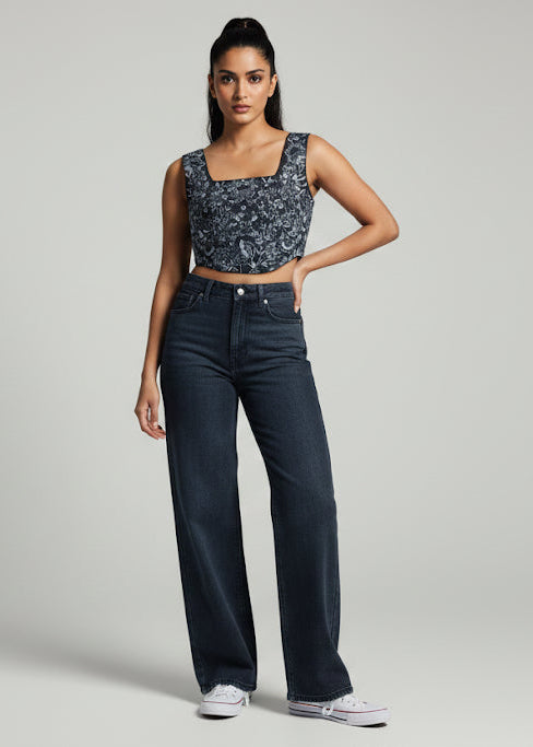Woman wearing a patterned top and dark jeans on a gray background