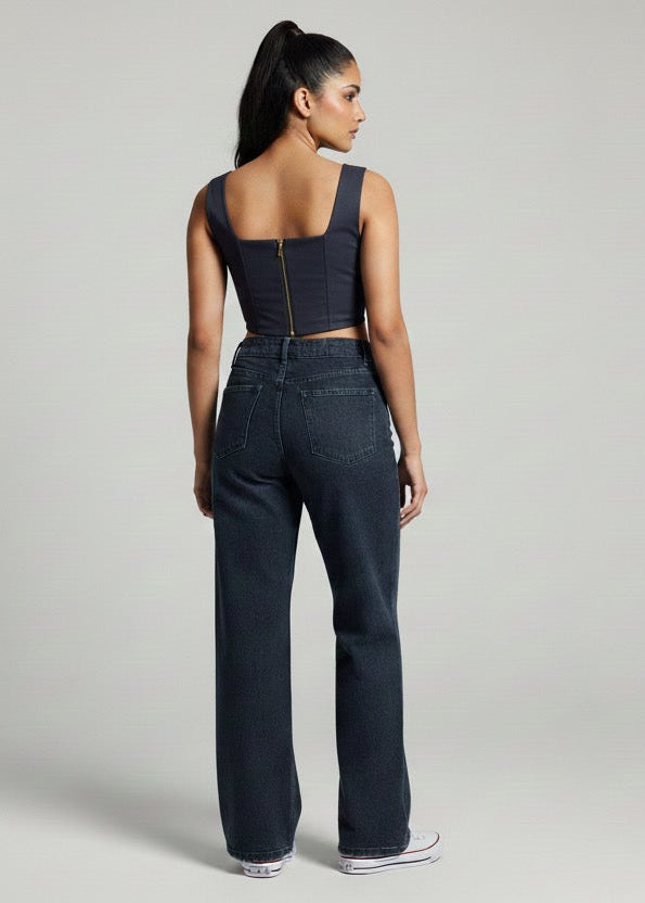 Woman wearing a black sleeveless top and dark jeans on a gray background