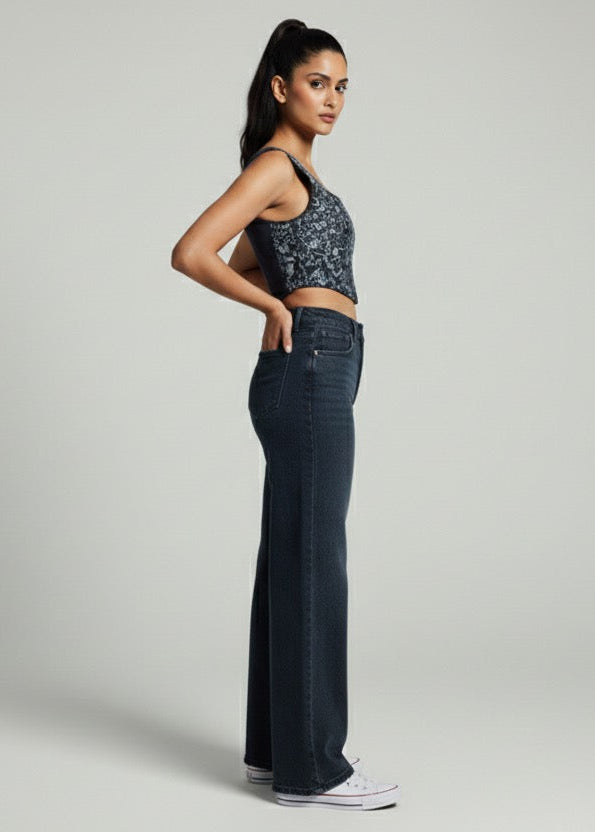 Woman wearing a crop top and dark jeans on a plain background