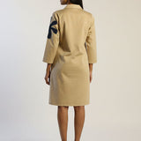 Woman wearing a beige suit with a black design on the back against a white background
