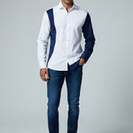 Man wearing a white shirt with navy accents and blue jeans on a gray background