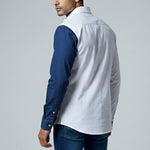 Man wearing a white shirt with blue sleeves and jeans on a gray background