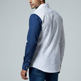 Man wearing a white shirt with blue sleeves and jeans on a gray background