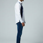 Man wearing a white shirt, dark vest, and blue jeans on a gray background