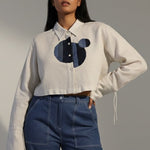 Woman wearing a white shirt with a black and blue design and blue jeans against a gray background