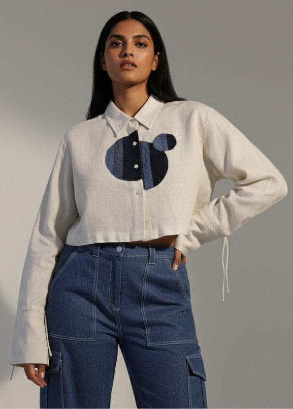 Woman wearing a white shirt with a black and blue design and blue jeans against a gray background