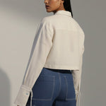 Woman wearing a white jacket and blue jeans against a plain background