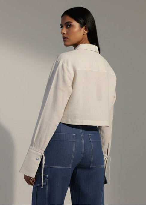 Woman wearing a white jacket and blue jeans against a plain background