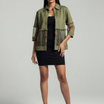 Woman wearing a green jacket over a black dress on a gray background