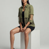 Woman sitting on a white cube wearing a green jacket and black shoes against a gray background
