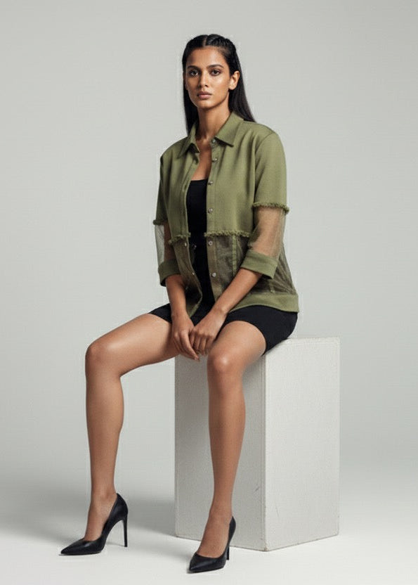 Woman sitting on a white cube wearing a green jacket and black shoes against a gray background