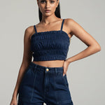 Woman wearing a navy blue crop top and high-waisted jeans against a gray background