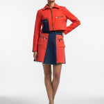 Woman wearing a red and navy jacket with a matching skirt on a white background