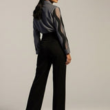Woman wearing a black outfit with sheer sleeves against a plain background