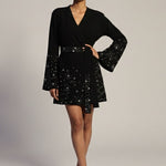 Woman wearing a black dress with star patterns on a plain background