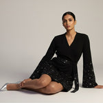 Woman wearing a black dress with sequin details on a plain background