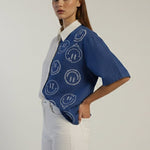 Woman wearing a blue patterned shirt with a white collar against a plain background
