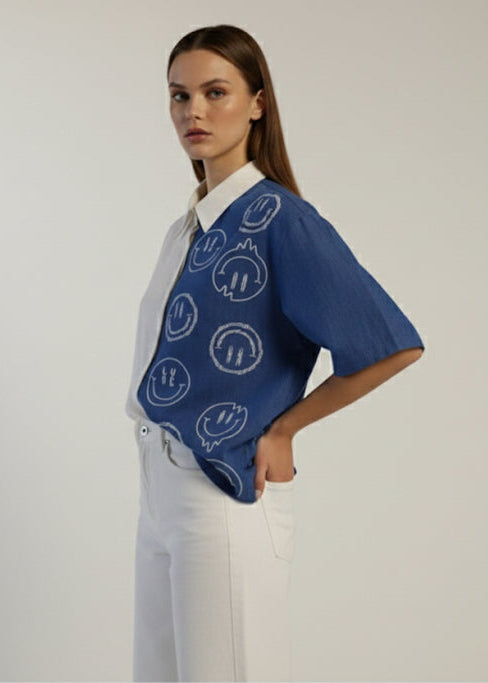 Woman wearing a blue patterned shirt with a white collar against a plain background