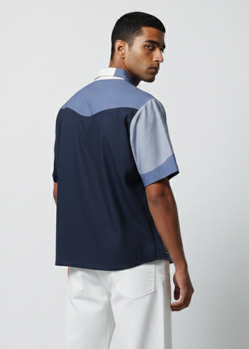 Man wearing a navy and light blue polo shirt with white pants on a plain background