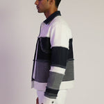 Man wearing a colorful striped sweater and white pants against a plain background