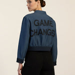 Person wearing a blue jacket with 'GAME CHANGER' text on the back, standing against a plain background.