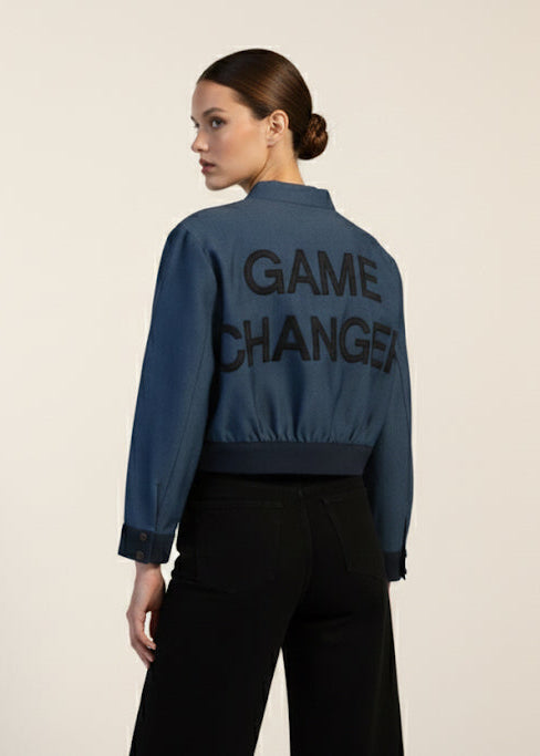 Person wearing a blue jacket with 'GAME CHANGER' text on the back, standing against a plain background.