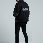 Man wearing a black jacket with text on the back against a gray background