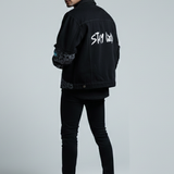 Man wearing a black jacket with text on the back against a gray background