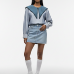 Woman wearing a blue and gray outfit with a denim skirt on a white background