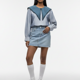 Woman wearing a blue and gray outfit with a denim skirt on a white background