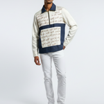 Man wearing a patterned sweater and white pants on a gray background