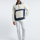 Man wearing a patterned sweater and white pants on a gray background