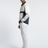 Man wearing a patterned shirt and light gray pants on a white background