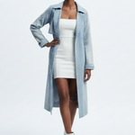 Woman wearing a light blue coat over a white dress on a plain background