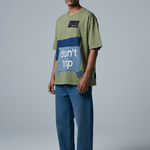 Man wearing a green t-shirt with a blue graphic and text, standing against a plain background