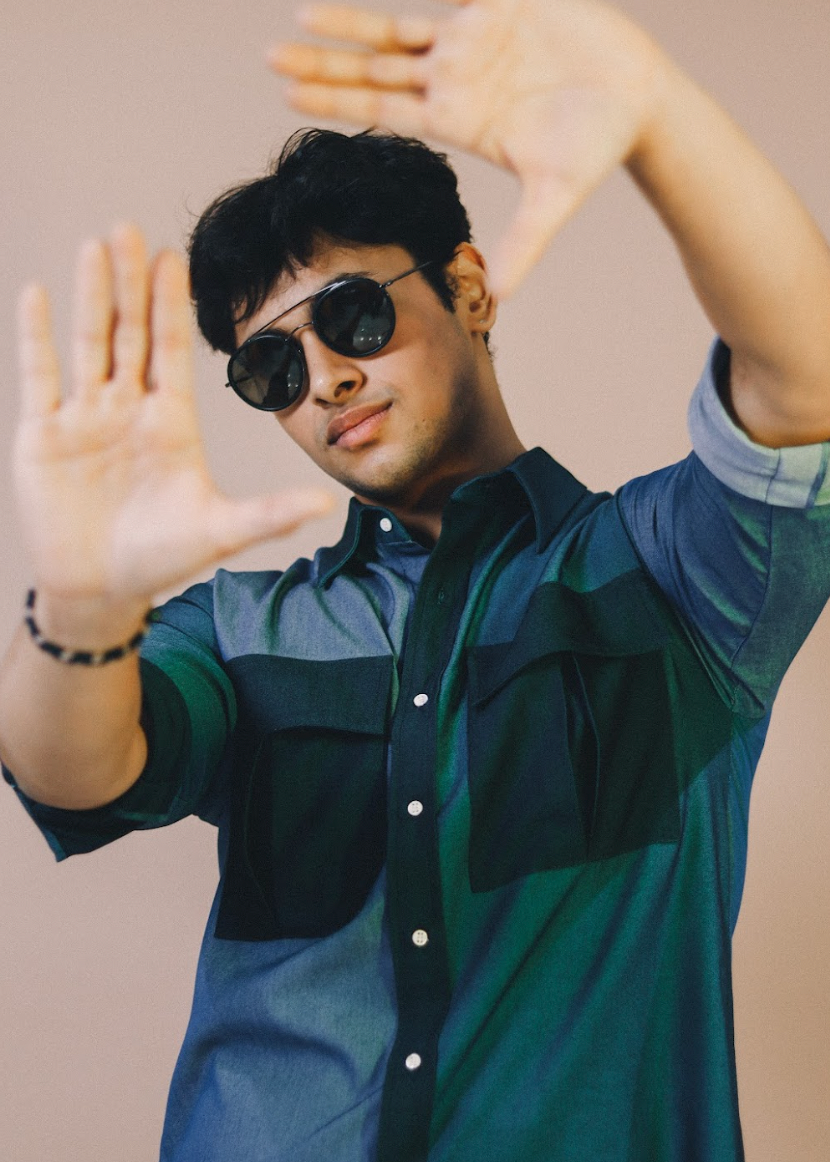 Man wearing sunglasses and a two-tone shirt with arms raised against a beige background