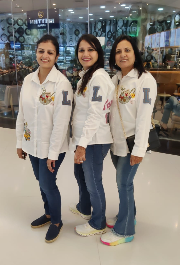 Three women wearing matching white jackets with a logo in a store setting.