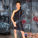 Woman in a black dress with unique sleeves standing against a graffiti-covered wall.