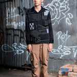 Person wearing a black jacket with geometric patterns in front of a graffiti-covered wall.