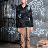 Person wearing a black jacket with geometric patterns in front of a graffiti-covered wall.
