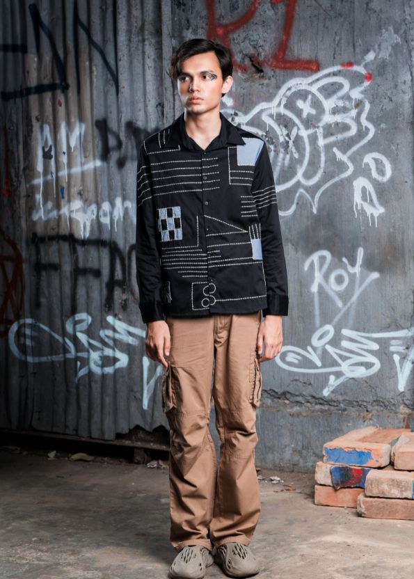 Person wearing a black jacket with geometric patterns in front of a graffiti-covered wall.