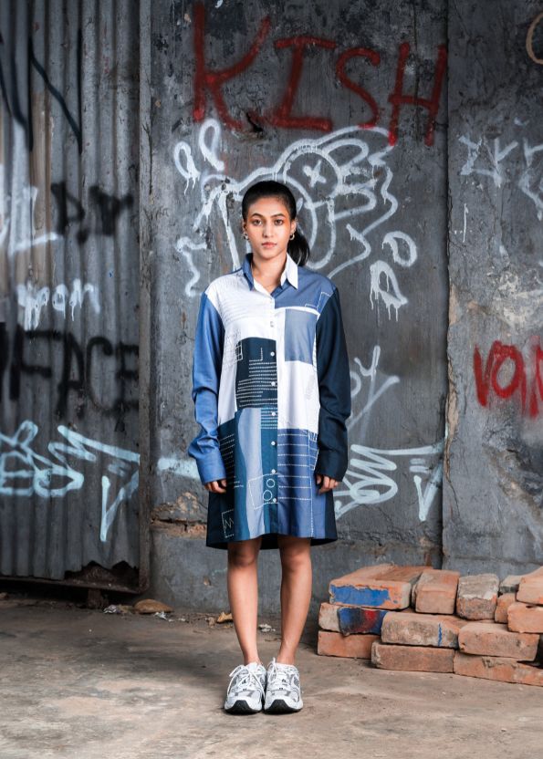 Person wearing a blue and white outfit standing in front of a graffiti-covered wall.